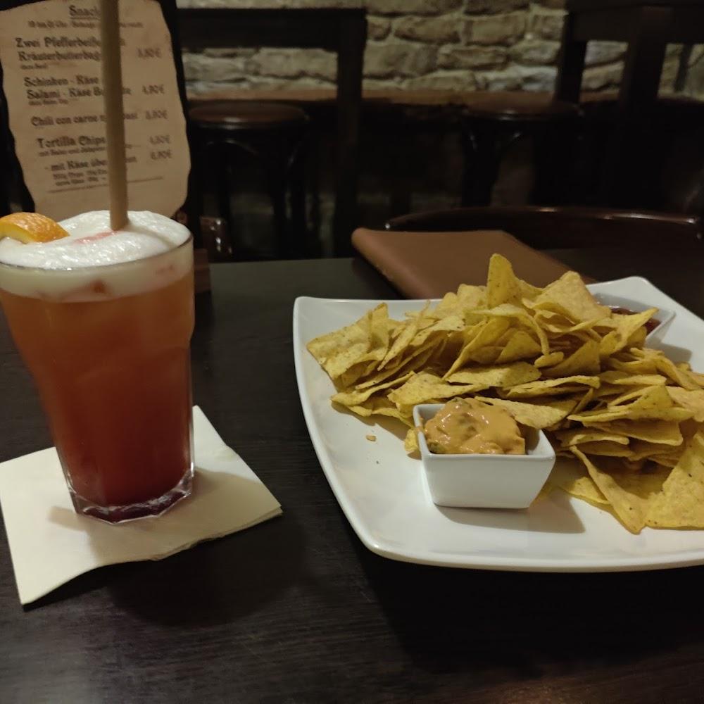A cocktail, nachos, and dip on a white plate.